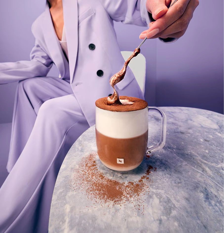 A person holding the new Signature Glass coffee cup against a soft pink backdrop.