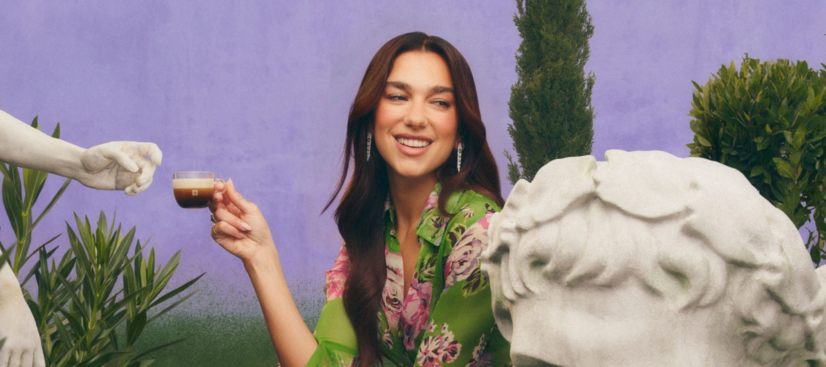 Dua Lipa reclining on pink cushions while holding a Bubblegum Pink Tumbler with iced coffee