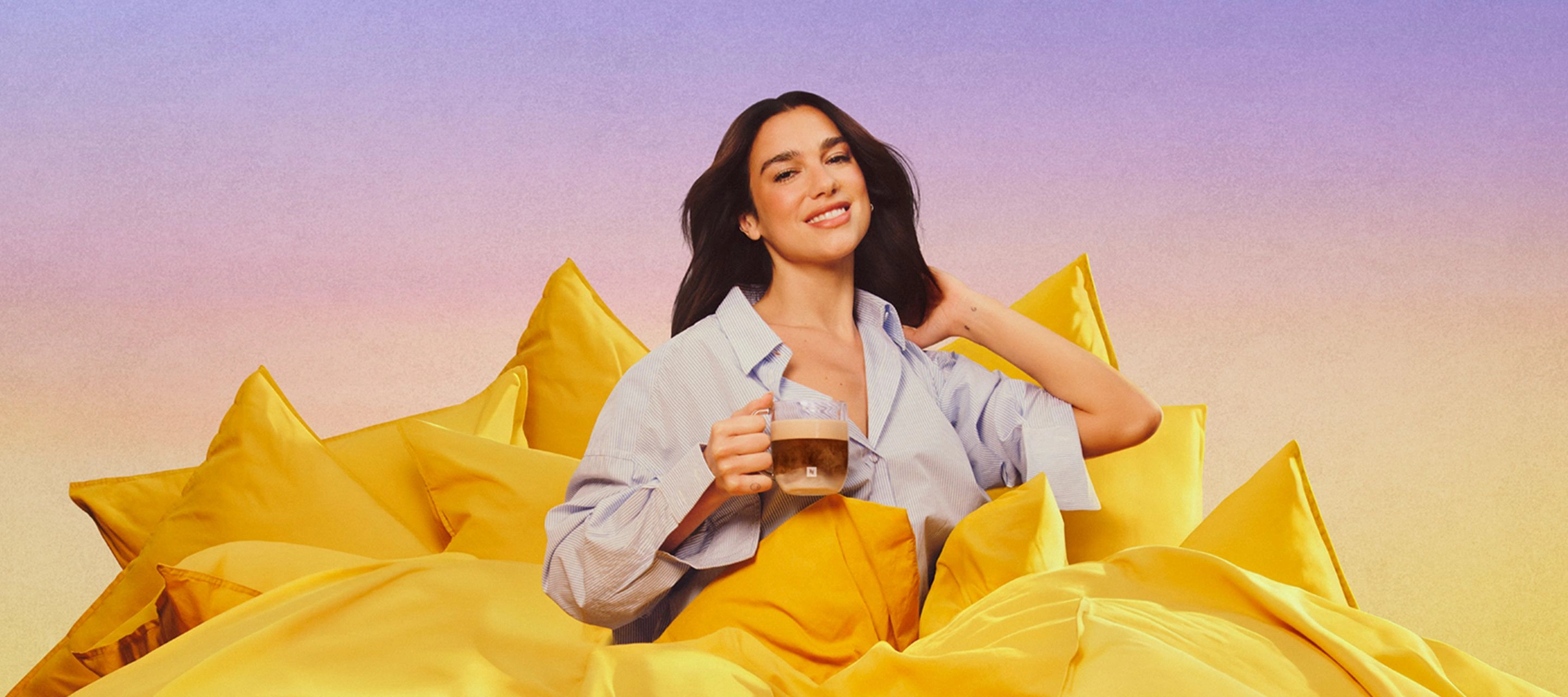 Dua Lipa reclining on pink cushions while holding a Bubblegum Pink Tumbler with iced coffee