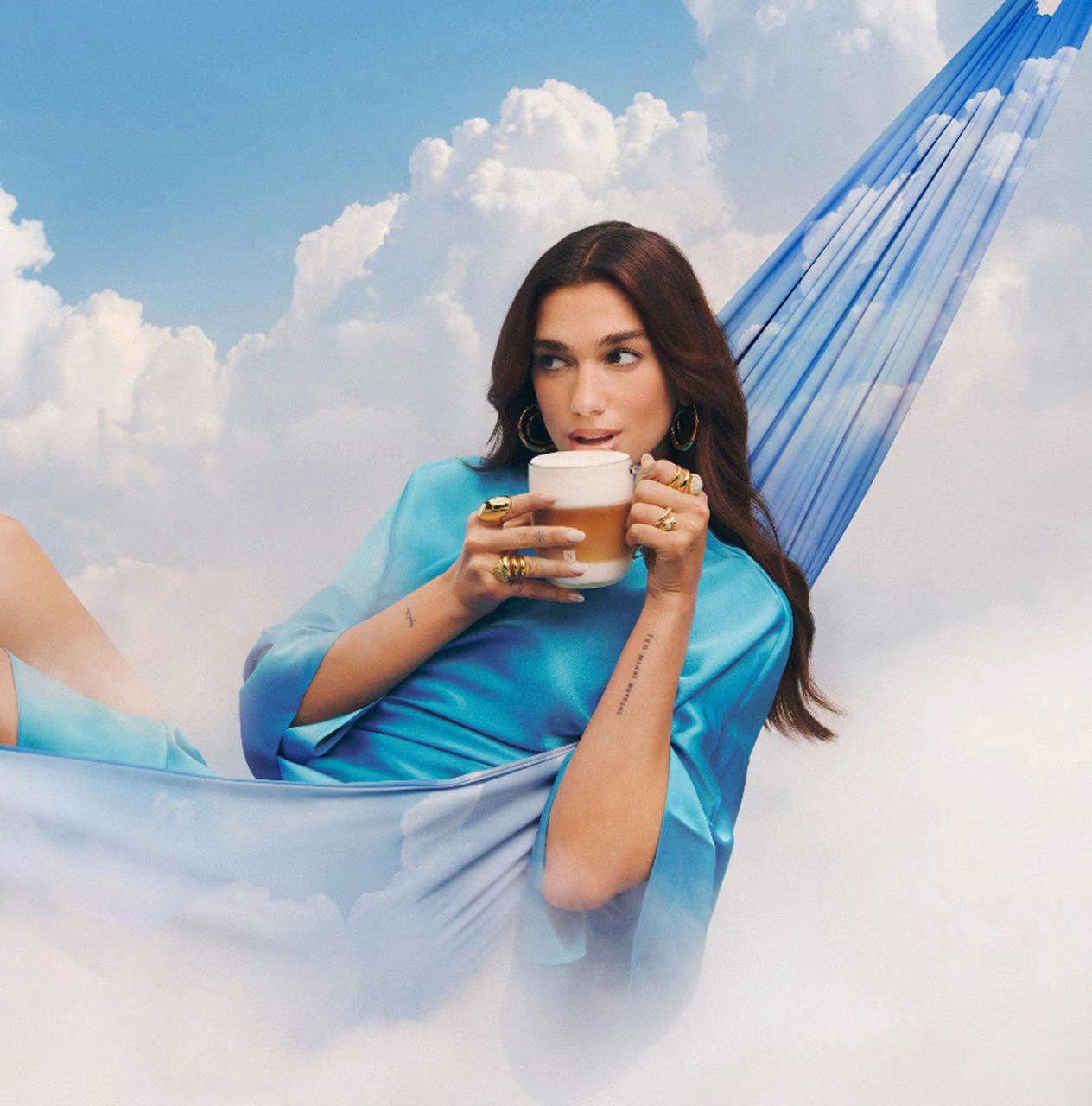 Dua Lipa reclining on pink cushions while holding a Bubblegum Pink Tumbler with iced coffee