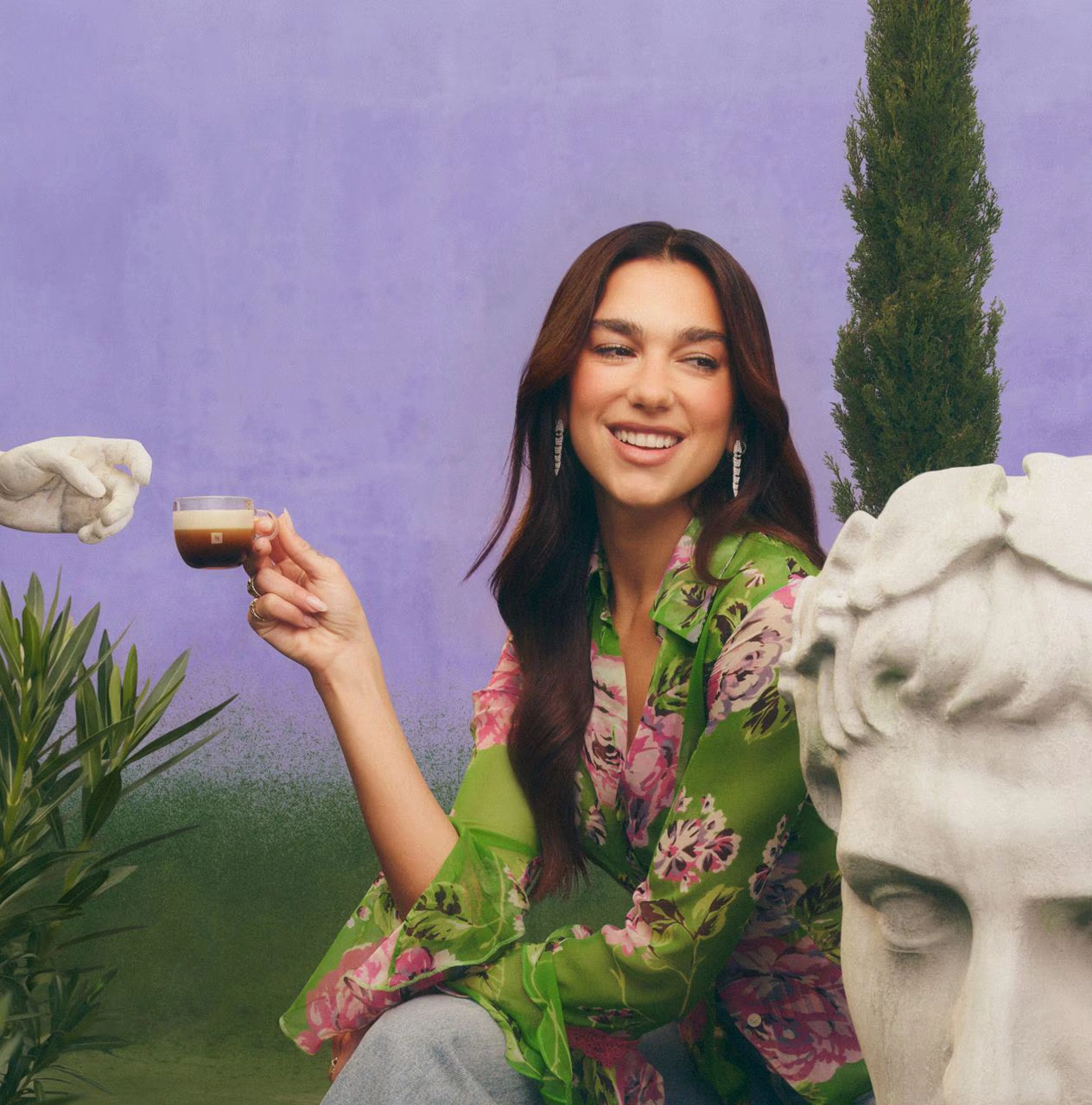 Dua Lipa reclining on pink cushions while holding a Bubblegum Pink Tumbler with iced coffee