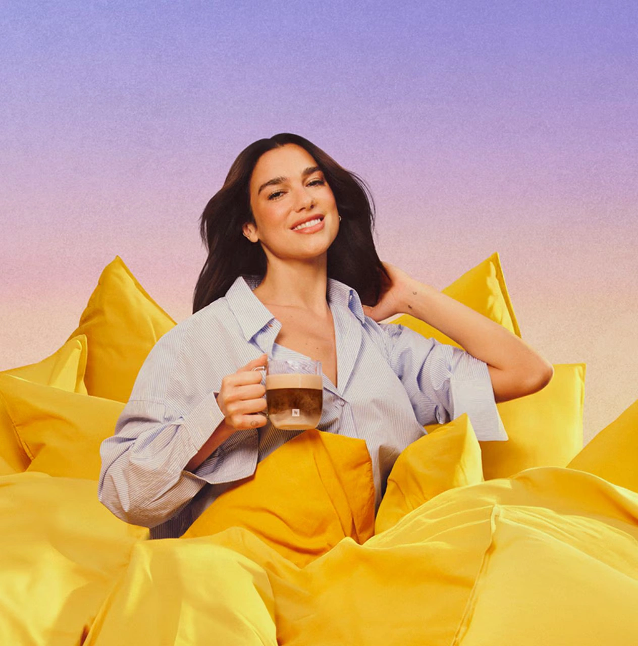 Dua Lipa reclining on pink cushions while holding a Bubblegum Pink Tumbler with iced coffee